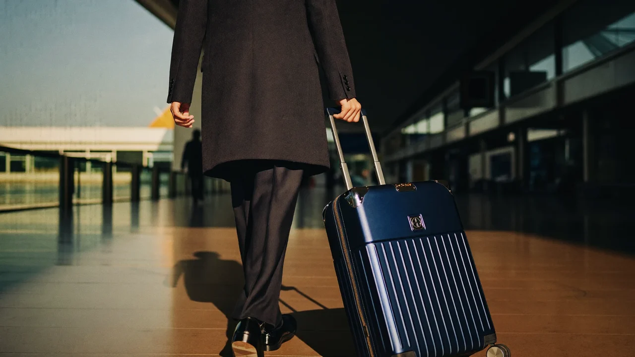 Voyageur de dos tirant une valise cabine dans un grand hall lumineux.